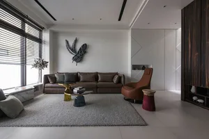A modern living room featuring a brown leather sofa, wooden armchair, glass coffee table, and a decorative wall hanging.