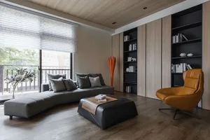 A modern living room with mixed materials, including a gray sectional sofa, a black ottoman, a brown leather chair, and a tal