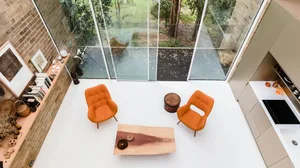A minimalist living room with orange chairs, a wooden table, and a bookshelf filled with books and decorative items.
