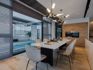 A modern residential kitchen featuring a large white marble dining table and chairs, with a view of an indoor pool.
