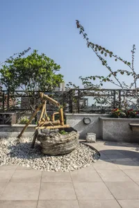 A serene outdoor space featuring a stone water bowl, bamboo water feature, and gravel pathway.