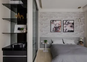 A minimalist bedroom with a brick accent wall, featuring a bed with gray bedding and a small table with a green plant.