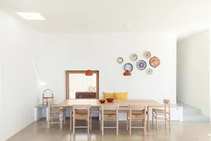 A minimalist dining room with a wooden table and chairs, yellow cushions, and decorative plates on the wall.
