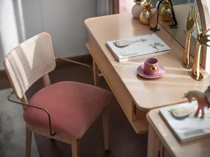 A modern home office featuring a wooden desk, pink chair, decorative items, and a book with a musical instrument illustration