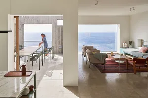 A modern residential interior with concrete walls, glass doors, and a view of the ocean.