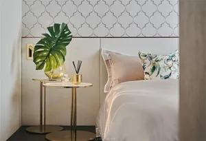 A minimalist bedroom with a bed dressed in white linen, a headboard with gold accents, and a bedside table featuring a gold v