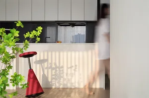 A minimalist kitchen area with a concrete countertop and a red stool.