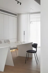 Modern, minimalist kitchen interior with white cabinets, counter, and seating area. Features sleek, clean design.