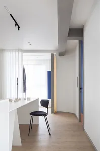 Modern living room with white concrete walls, wooden flooring, and minimalist furnishings.