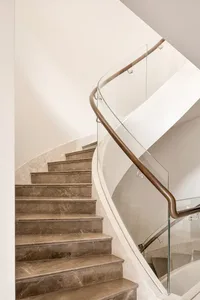 Curved, modern marble staircase with a glass and wooden handrail.