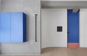 A minimalist interior with a blue-cabinet, light wooden floor, and a red and blue door with a black panel.
