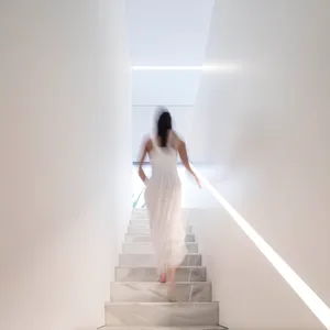 A woman in a white dress walking up a staircase made of white marble.