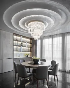 A modern dining room with mixed materials, including a round table, gray chairs, and a crystal chandelier.