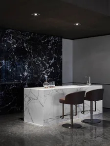 Modern kitchen with white marble countertop and black marble backsplash, featuring a single water faucet and two bar stools.