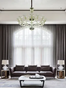 A modern living room with a dark leather sofa, glass coffee table, and metal side tables. The room features large windows wit