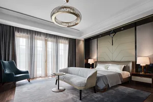 A modern residential bedroom with grey fabric furniture, wooden accents, and a sleek glass lighting fixture.