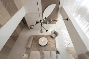 A modern minimalist living room with light-colored furniture, a white marble coffee table, and a large window allowing natura