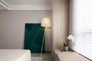 Modern minimalist bedroom with a white bed, green abstract artwork, white floor lamp, and light wood bench and walls.