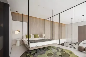 Modern minimalist bedroom featuring a floating bed, green accent pillows, and a green and gray rug with abstract circular pat