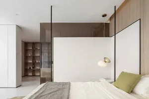 A minimalist bedroom with white walls, a bed, green pillow, and a glass partition.