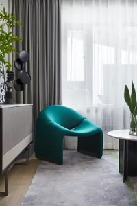 A modern living room with a green armchair, grey curtains, and a round marble table.