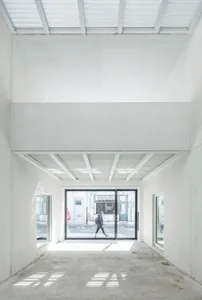 A minimalist retail space with concrete walls and floor, large glass doors and windows.