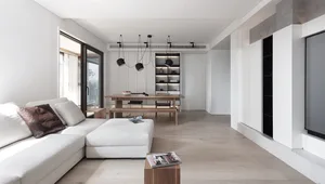 Modern minimalist living room with white furniture, wooden flooring, and floating shelves.