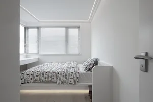 A modern bedroom with a bed, window, and wooden floor.