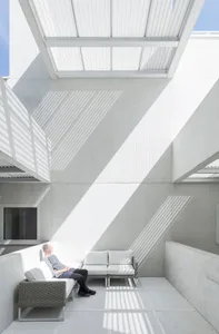 A minimalist interior space with concrete walls and a concrete floor, featuring white furniture and a television.
