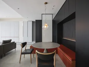A modern minimalist indoor space featuring a concrete table and chairs, black and red seating, and a glass pendant light hang