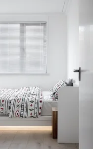 Minimalist bedroom with white walls, wooden floor, and patterned bedding.