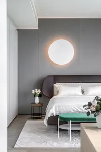 Minimalist bedroom featuring a round wall sconce and a wooden headboard on a bed with soft textiles.