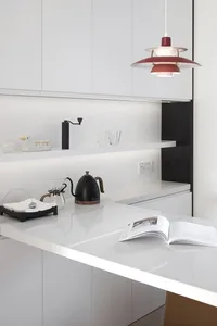Modern minimalist kitchen with sleek white marble countertops and cabinets, featuring a minimalist pendant light fixture.