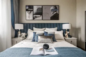 A modern bedroom featuring a bed with a blue upholstered headboard, white and gray bedding, and a variety of decorative pillo