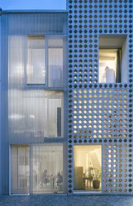A modern building facade with metallic panels and a grid-like pattern, featuring illuminated windows and a clean, contemporar
