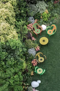 A modern garden with metallic and plastic furniture, surrounded by lush greenery and colorful flowers.