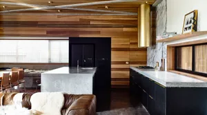 Modern kitchen and dining area featuring concrete countertops, wooden walls, marble flooring, and metal accents.
