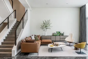 A modern living room with a brown leather couch, white coffee table, and minimalist decor.
