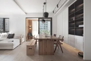 A modern living room featuring a contemporary sofa, large windows, minimalist design, and a natural wood dining table.
