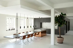 A modern minimalist kitchen with a concrete floor, long dining table, and dark cabinets.