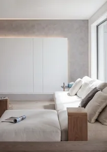A minimalist living room with a white sofa, neutral-toned cushions, and a wooden ottoman in a neutral-toned space.