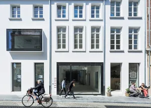 Modern street view featuring a coffee shop with glass and concrete facade, people walking by, and a cyclist.