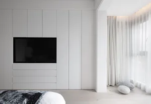 A minimalist bedroom with white furniture and a television on the wall.