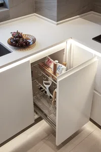 A modern, minimalist kitchen with white cabinetry, featuring an organized drawer and a countertop with grapes and a bowl.