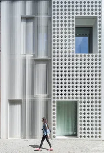 Person walking past a modern building with concrete texture and geometric patterns on the facade.