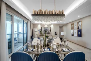 Modern dining room with metal and glass furniture, chandelier, and blue chairs.