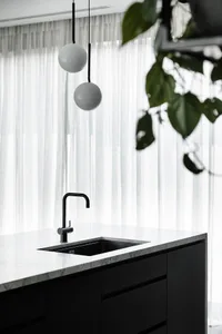 Modern kitchen with black and white marble countertops, black sink, and hanging white globe lights. White sheer curtains and 