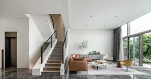 A modern minimalist living room with a brown leather sofa, white coffee table, and large windows.