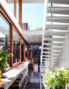 A modern, minimalist staircase with white steps, surrounded by indoor plants and a floor-to-ceiling window.