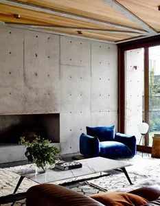 A modern industrial living room with concrete walls, a blue velvet armchair, and a marble coffee table.